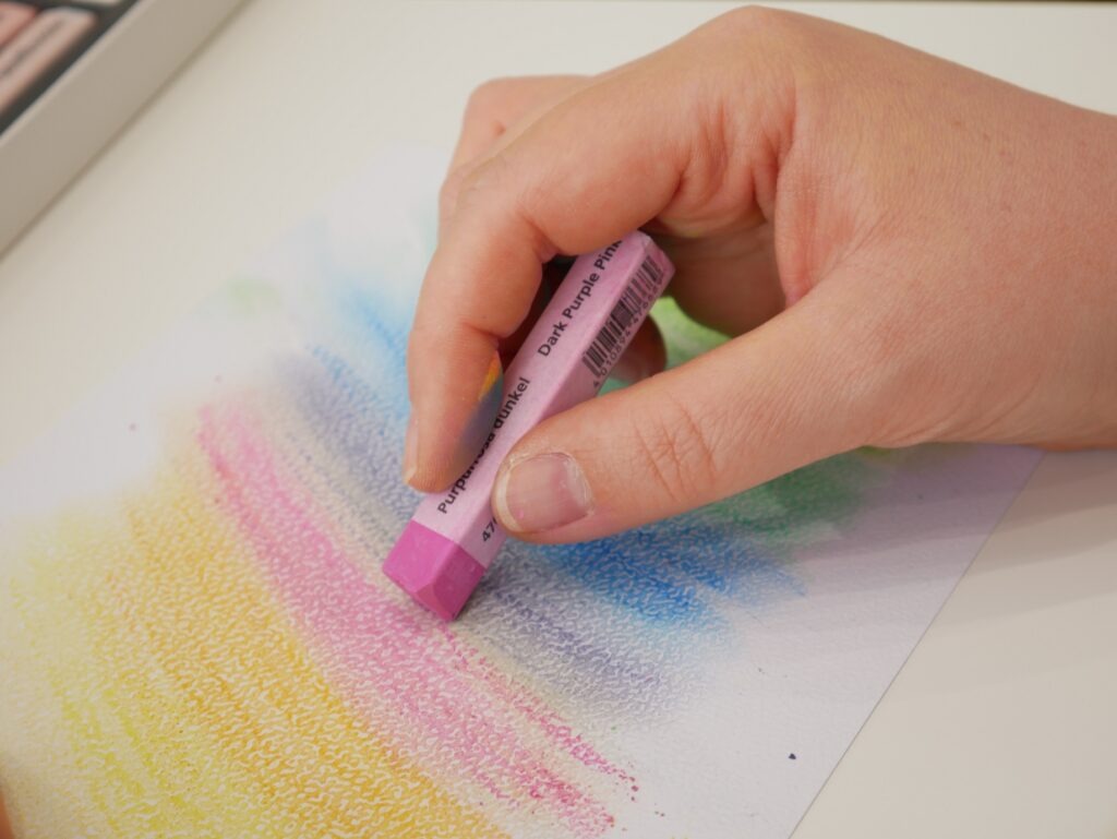 Ein Blatt Papier bemalt mit Aquarellkreide in bunten Farben.
