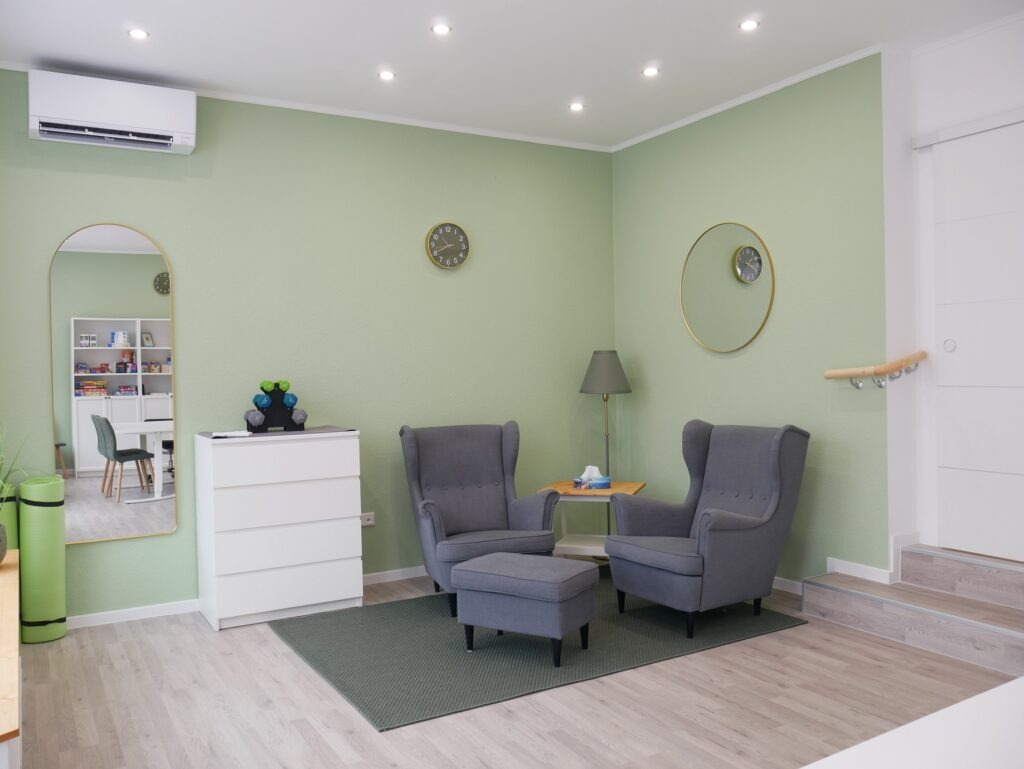Sitzecke Praxis für Ergotherapie in Dreieich mit gemütlichen Sesseln, einer Kommode mit Sensorikmaterial, Trainingsmatte und Gewichte zur körperlichen Aktivierung